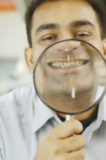 Indian man holding up magnifying glass to his teeth with braces