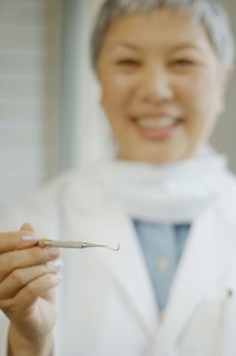 Senior Asian female dentist holding up dental tool