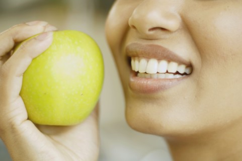 Close up of woman holding apple next to her mouth