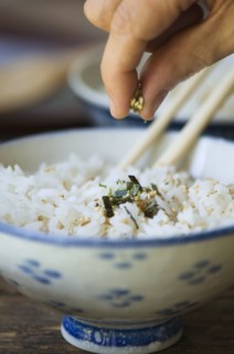 Hand putting seasoning on bowl of rice with chopsticks