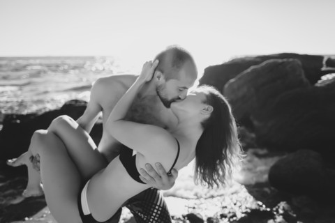 Caucasian man carrying and kissing woman on beach