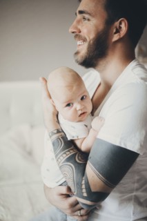 Caucasian father with tattoos on arms holding baby son