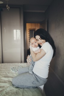 Caucasian mother kneeling on bed hugging baby son