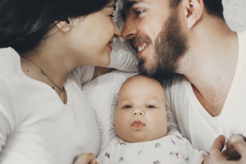 Caucasian mother and father laying on bed with baby son