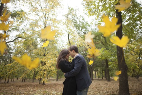 Autumn leaves falling near hugging Caucasian couple