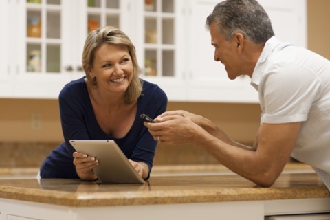 Caucasian couple using digital tablet and cell phone at kitchen counter
