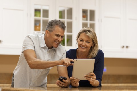 Caucasian couple using digital tablet and cell phone at kitchen counter