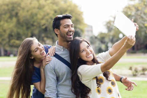 Smiling friends taking photograph with digital tablet in park