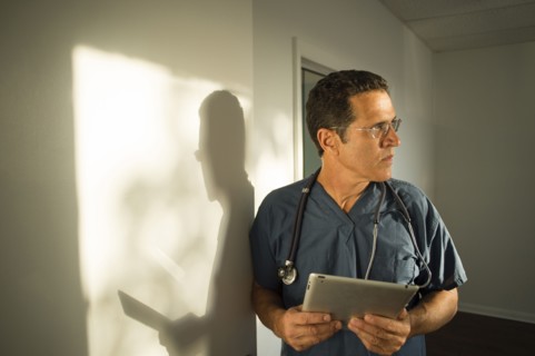 Hispanic doctor leaning on wall using digital tablet