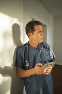 Hispanic doctor leaning on wall using cell phone