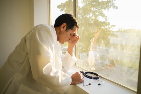 Stressed Hispanic doctor standing at window