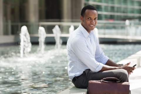 Black businessman using cell phone near urban fountain