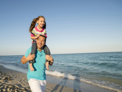 Hispanic father carrying daughter on shoulders on beach