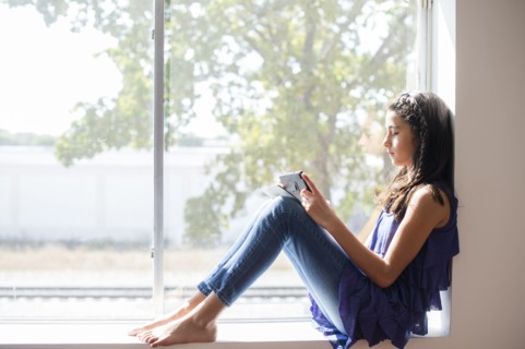 Mixed race girl using digital tablet at window