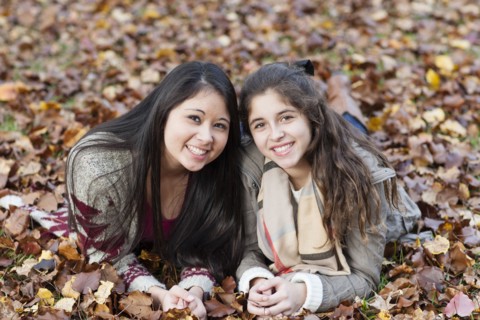 Hispanic sisters laying in autumn leaves