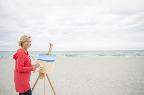 Older Caucasian woman painting on beach