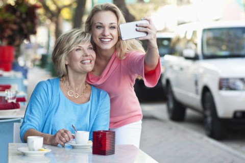 Caucasian mother and daughter taking selfie at sidewalk cafe