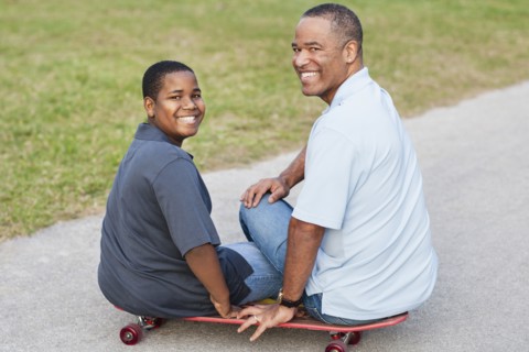 African American father and son sitting on skateboard on path
