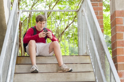 Caucasian teenage boy using cell phone on steps