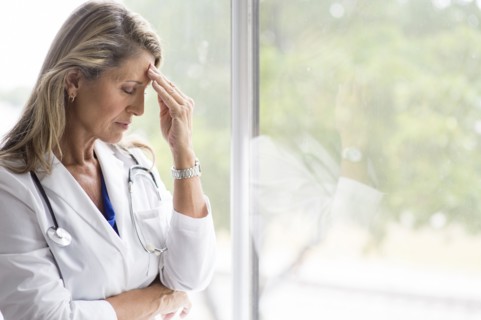 Caucasian doctor rubbing forehead at window