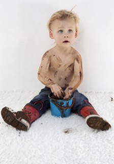 Messy Caucasian boy playing with mud on white carpet