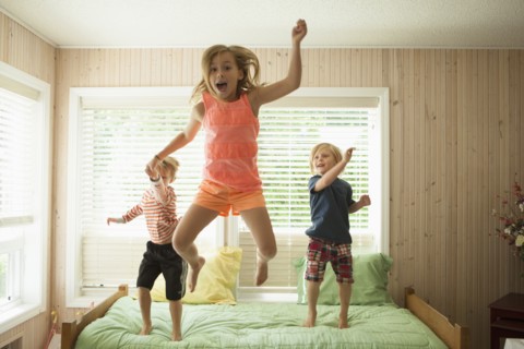 Caucasian children jumping on bed