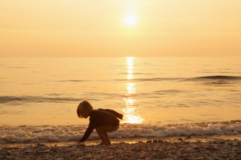 Caucasian boy playing on rocky beach at sunset