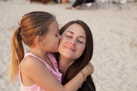 Caucasian girl kissing cheek of mother on beach