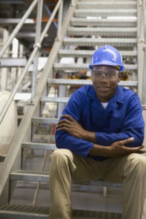 African worker in hard-hat sitting on metal staircase