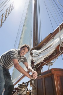 Caucasian man hoisting sail on sailboat