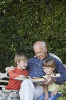 Grandfather reading to grandchildren on garden bench