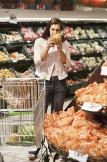 Caucasian woman smelling pineapple in grocery store