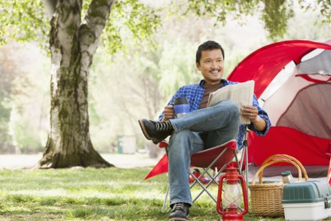 Asian man relaxing in lawn chair at campsite