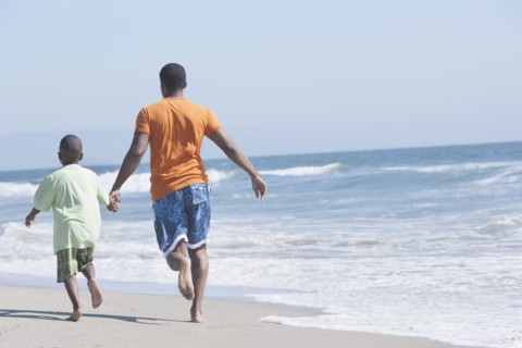Father and son walking in waves on beach