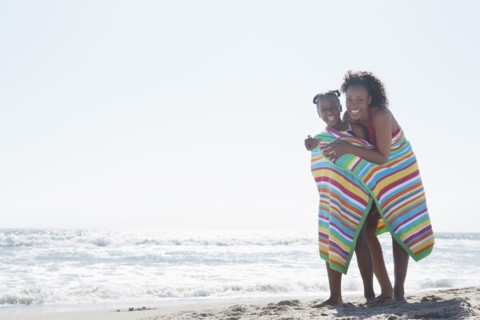 Mother and daughter wrapped in towel on beach
