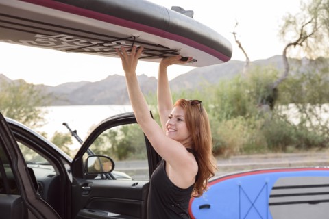 Caucasian woman lifting paddleboard from roof of car