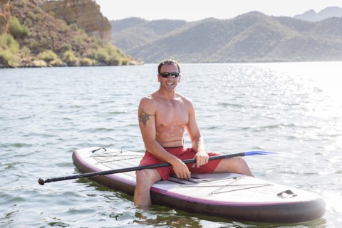 Hispanic man sitting on paddleboard in river