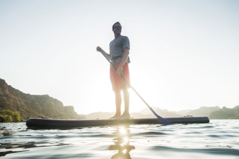 Smiling Hispanic man standing on paddleboard in river