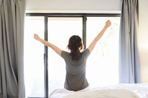 Caucasian woman sitting on bed stretching arms