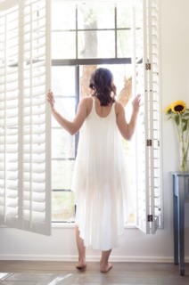 Caucasian woman wearing nightgown opening window shutters