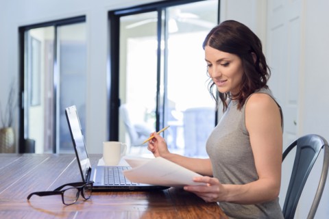 Caucasian woman reading paperwork and using laptop