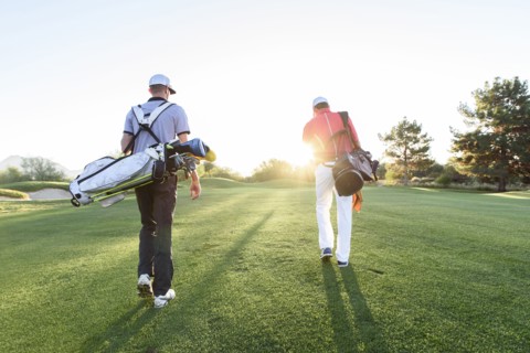 Men carrying golf bags on sunny golf course