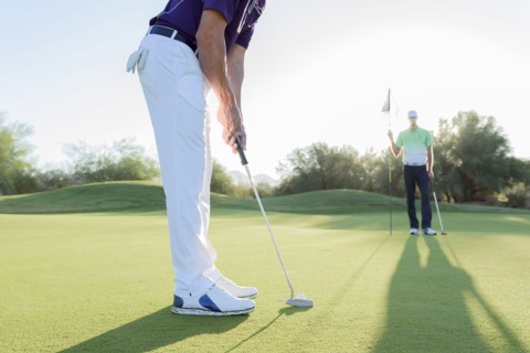 Hispanic man watching friend putting on golf course