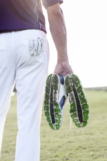 Hispanic man hold golf shoes covered with grass