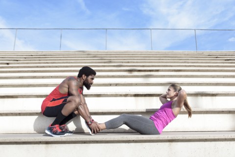 Man holding feet of woman doing sit-ups on bleachers