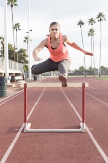Hispanic woman jumping over hurdle