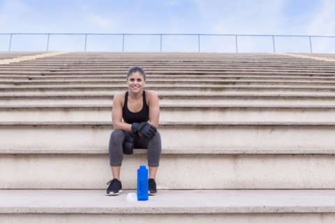 Hispanic woman wearing boxing gloves resting on bleachers