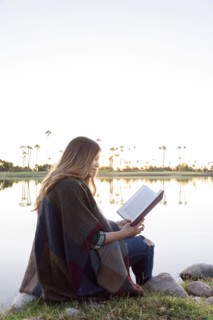 Hispanic woman sitting bear lake reading book