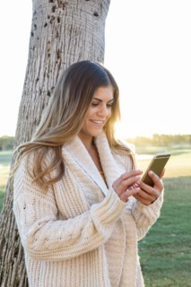Hispanic woman leaning on tree texting on cell phone