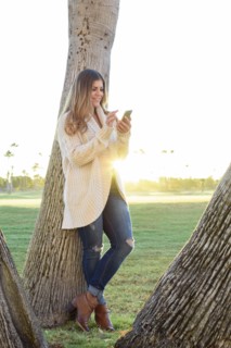 Hispanic woman leaning on tree texting on cell phone